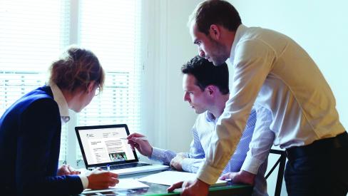 Three people working together and looking at a computer screen.